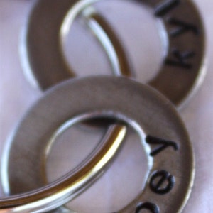 May include: Two silver metal rings with the words "Kelly" and "Joey" engraved on them. The rings are connected by a silver metal chain.