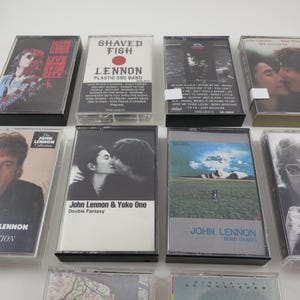 May include: A collection of eight cassette tapes featuring music by John Lennon. The tapes are in clear plastic cases with black and white photos of John Lennon and Yoko Ono on the covers. The titles of the tapes include "Shaved Fish", "Double Fantasy", "Mind Games", and "The John Lennon Collection".
