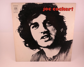 May include: A black and white photo of Joe Cocker on a white vinyl record album cover. The album title is "Joe Cocker!" in red letters.