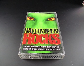May include: A cassette tape with a green and red design. The text "HALLOWEEN ROCKS" is printed in red on the front of the cassette. The text "FEATURING "MONSTER MASH" BY BOBBY "BORIS" PICKETT AND HAUNTED HITS BY KISS, DAVID BOWIE, CREAM AND DEEP PURPLE" is printed in black on the front of the cassette.