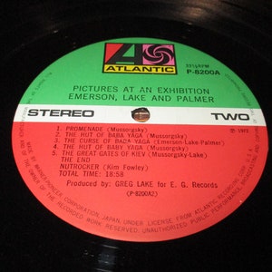 Op de afbeelding: Een rood en wit vinyl platenlabel met de tekst "Pictures at an Exhibition Emerson, Lake and Palmer" en "Stereo" in zwart. Het label bevat ook de tekst "Two" en "1972" in wit. Het platenlabel is groen aan de buitenrand.