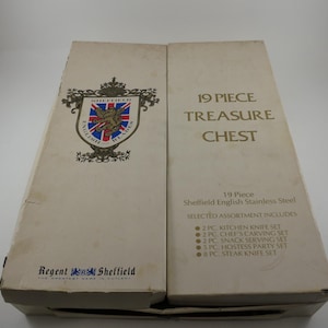 May include: A cream-colored box labeled "19 PIECE TREASURE CHEST" with text and a crest. The box is for a 19-piece Sheffield English Stainless Steel set, including kitchen knives, carving sets, and steak knives.