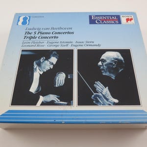 May include: A vintage CD case for Ludwig van Beethoven's "The 5 Piano Concertos Triple Concerto." The cover features black and white portraits of musicians and the "Essential Classics" logo. The case is blue and white.