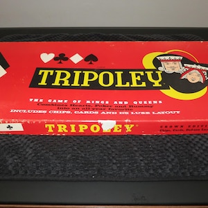May include: A rectangular red board game box for Tripoley Crown Edition No. 229. The box features the text Tripoley, The Game of Kings and Queens, and includes chips, cards, and de luxe layout. It displays card suit symbols and king and queen illustrations.