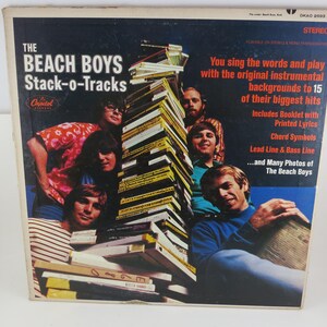 May include: Vintage vinyl record album cover for "The Beach Boys Stack-o-Tracks." The cover features a photo of the band members and text that reads "You sing the words and play with the original instrumental backgrounds to 15 of their biggest hits."