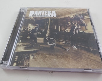 May include: A CD case featuring the album "Cowboys from Hell" by Pantera. The cover art depicts a sepia-toned image of a band performing in a saloon. The band's name is in bold white letters at the top.