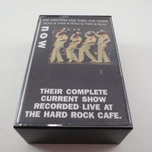 May include: A black cassette tape with a photo of The Drifters on the front. The text on the front reads "The Drifters Live Thru The Years Now & Then & Now & Then & Now" and "Their Complete Current Show Recorded Live At The Hard Rock Cafe."