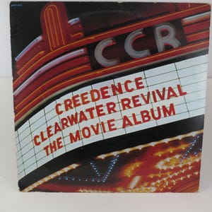 May include: Vintage vinyl record album cover for Creedence Clearwater Revival's "The Movie Album." The cover features a retro movie theater marquee design with the band's name and album title in red and white lettering against a black background.
