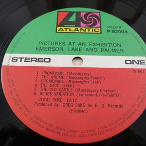 Puede incluir: Un disco de vinilo del &aacute;lbum "Pictures at an Exhibition" de Emerson, Lake and Palmer. La etiqueta del disco es verde y roja con el logotipo de Atlantic Records. La lista de canciones incluye "Promenade" y "The Gnome".