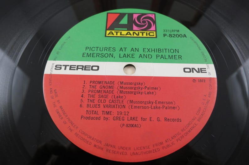 Puede incluir: Un disco de vinilo del &aacute;lbum "Pictures at an Exhibition" de Emerson, Lake and Palmer. La etiqueta del disco es verde y roja con el logotipo de Atlantic Records. La lista de canciones incluye "Promenade" y "The Gnome".