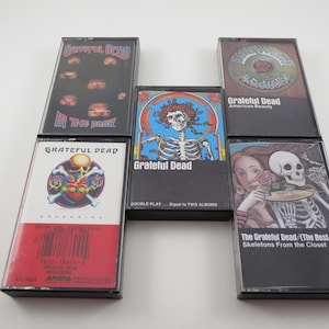 May include: A collection of eight cassette tapes featuring the Grateful Dead band. The tapes are black with various images and text, including "Grateful Dead", "American Beauty", "Skeletons From the Closet", and "Double Play - Equal to Two Albums".
