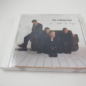 Puede incluir: Una caja de CD con una foto de la banda The Cranberries en la parte delantera. Los miembros de la banda est&aacute;n sentados en un sof&aacute; y el texto "no need to argue" est&aacute; impreso en la parte delantera de la caja.