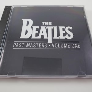 May include: A CD case for "The Beatles: Past Masters, Volume One." The album cover is black with white text. The band's name is in large, bold letters. The CD case is clear plastic.