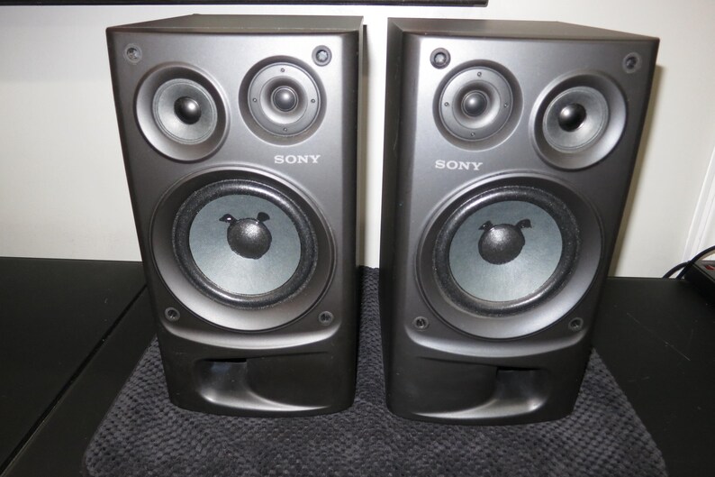 May include: A pair of black Sony bookshelf speakers featuring a two-way design with a large woofer, a smaller tweeter, and a bass reflex port at the bottom. The Sony logo is printed in white on the front of each rectangular speaker cabinet.