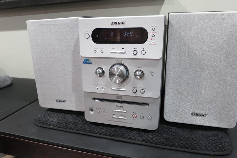 May include: A silver and white Sony stereo system with two speakers. The stereo has a digital display, CD player, and various control buttons. The speakers are rectangular and have the Sony logo.