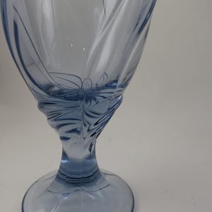 Pu&ograve; includere: Un calice di vetro blu chiaro con un design a spirale dettagliato. Lo stelo e la base sono solidi, mentre la coppa presenta un delicato motivo inciso. Il vetro ha una superficie liscia e riflettente.