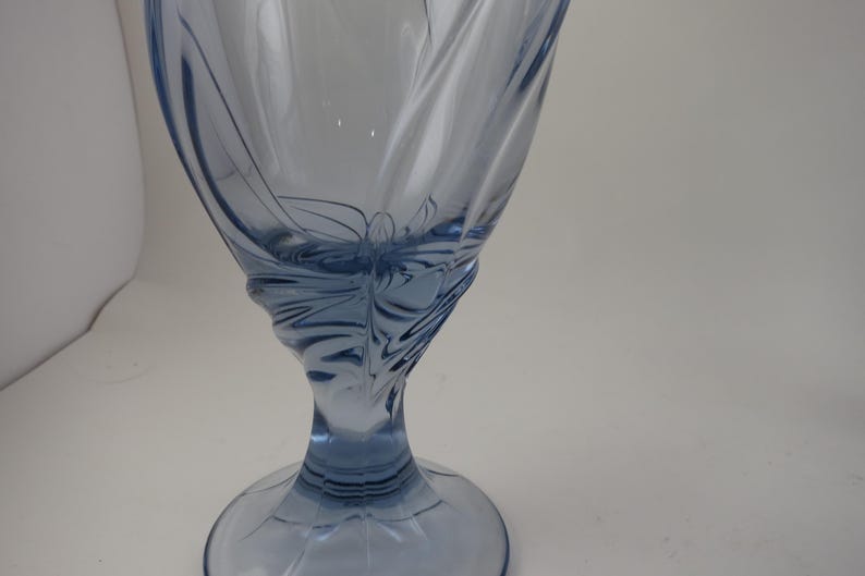Pu&ograve; includere: Un calice di vetro blu chiaro con un design a spirale dettagliato. Lo stelo e la base sono solidi, mentre la coppa presenta un delicato motivo inciso. Il vetro ha una superficie liscia e riflettente.