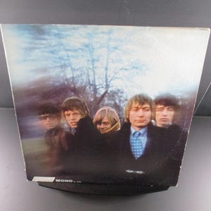 May include: A vintage vinyl record album cover featuring a band of five men in black and white clothing. The album cover is a blurred image of the band standing in front of a tree line. The album title is "MONO" in the bottom right corner.