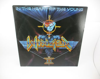 Könnte beinhalten: Ein schwarzes Vinyl-Albumcover mit dem Titel "In the Heart of the Young" der Band "Winger". Das Cover zeigt ein futuristisches Design mit einem metallischen Raumschiff und einer kybernetischen Figur mit leuchtend roten Augen.