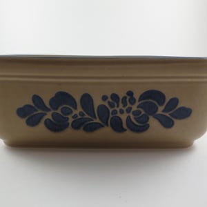 May include: Tan rectangular baking dish with blue floral design. The dish has a slightly flared shape and small handles on each end. The blue floral pattern is centered on the front of the dish.