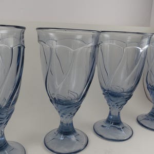 Pu&ograve; includere: Quattro bicchieri a stelo azzurri. I bicchieri hanno una coppa a forma di tulipano con un motivo decorativo e una base arrotondata. I bicchieri sono realizzati in un materiale di vetro trasparente.