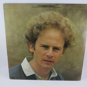 May include: Album cover featuring a man with curly blonde hair and a blue shirt with a white collar. The album is labeled "AMERICA" at the top left and "SQ QUADRAPHONIC" at the top right.