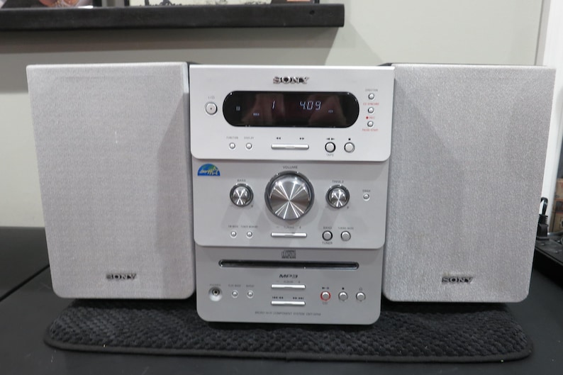 May include: A silver Sony stereo system with two speakers. The stereo has a CD player, radio, and display screen showing the time. The speakers and stereo are silver and have the Sony logo.