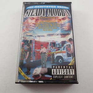 May include: A cassette tape case featuring the album art for "Steady Mobbin' Pre-Meditated Drama." The cover art includes images of two men, a fire truck, and a crime scene. The case has a "Parental Advisory Explicit Content" warning.