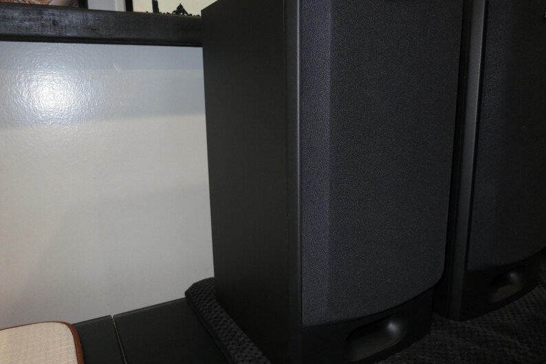 May include: Two black tower speakers with a textured front panel. The speakers are rectangular with rounded edges and sit on a black base. The speakers are designed for home audio systems.