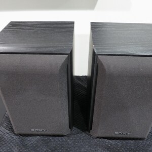 May include: A pair of black Sony bookshelf speakers with a wood grain top finish and grey fabric speaker grilles. Each rectangular speaker unit features the Sony brand name printed in silver lettering at the bottom center of the front panel.