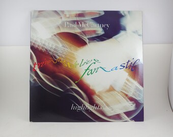 May include: Album cover for Paul McCartney's "Tripping the Live Fantastic: Highlights!" featuring a blurred image of a guitar. The album title and artist name are in white and the word "fantastic" is in rainbow colors.