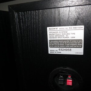 May include: Black speaker cabinet with a textured wood grain finish. A white label displays "SONY" and model information, including "SS-MB150H" and "SPEAKER SYSTEM." The back features a red and black connector.