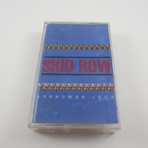 May include: A blue cassette tape case with the band name "SKID ROW" in red letters and the album title "SUBHUMAN RACE" in white letters.