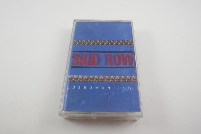 May include: A blue cassette tape case with the band name "SKID ROW" in red letters and the album title "SUBHUMAN RACE" in white letters.