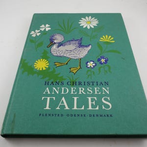 May include: A teal-colored book titled "TALES" by Hans Christian Andersen. The cover features a drawing of a duckling with floral illustrations. The book's origin is noted as Flenssted, Odense, Denmark.