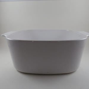 May include: A rectangular, off-white baking dish with two small handles on either side. The dish has a slightly rounded base and straight sides. The overall shape is a simple, functional design, suitable for oven use.