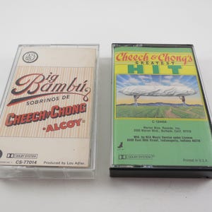 May include: Two vintage cassette tapes. One features the text "Big Bambu" and "Cheech & Chong" in red and black on a beige background. The other tape is green and yellow with "Cheech & Chong's Greatest Hit" and a landscape image.