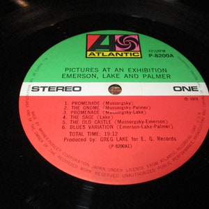 Op de afbeelding: Een rood en wit vinyl platenlabel met de titel "Pictures at an Exhibition" van Emerson, Lake and Palmer. De plaat is van Atlantic Records en is gelabeld "Stereo" en "E&eacute;n".