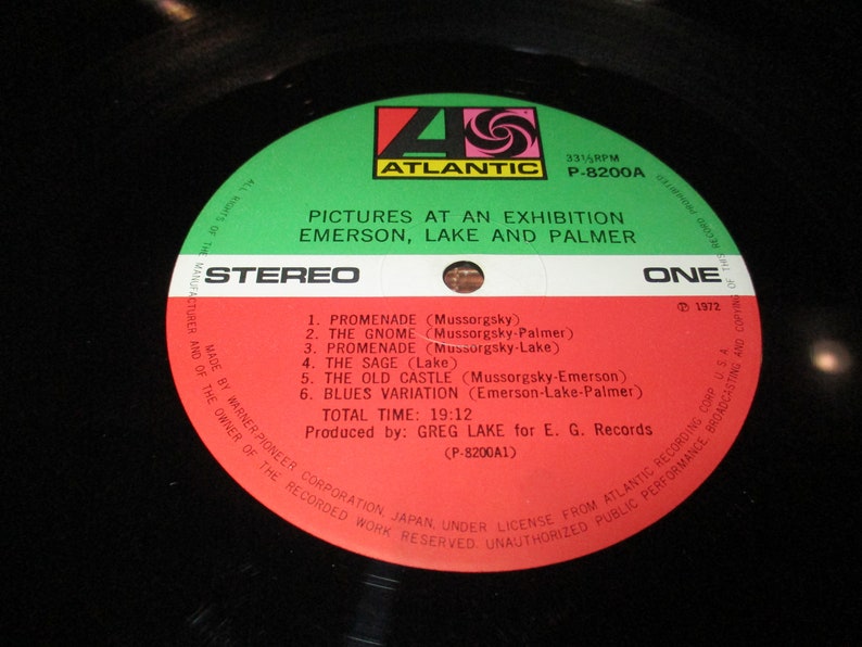 Op de afbeelding: Een rood en wit vinyl platenlabel met de titel "Pictures at an Exhibition" van Emerson, Lake and Palmer. De plaat is van Atlantic Records en is gelabeld "Stereo" en "E&eacute;n".