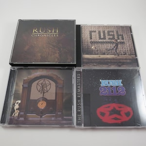 May include: Four CD cases featuring the Canadian rock band Rush. The cases are black with clear plastic inserts. The top case features the band's name and the words "Chronicles" in gold lettering. The second case features the band's name in white lettering on a black background. The third case features a radio with a star in the background. The fourth case features the band's name and the words "2112" in purple lettering.