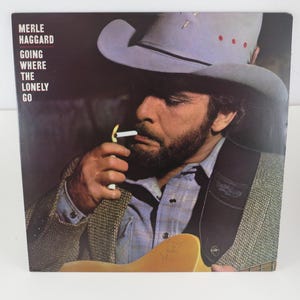 May include: Album cover for Merle Haggard's "Going Where the Lonely Go." The image features a man in a cowboy hat, smoking a cigarette. The album cover has a dark background with the album title and artist's name.