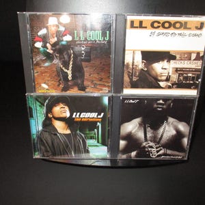 May include: Four CD cases with black borders and clear plastic fronts. The cases feature different album covers by LL Cool J. The album covers feature LL Cool J in various poses and settings. The album titles are "14 Shots to the Dome", "Walking with a Panther", "The Definition", and "LL Cool J".