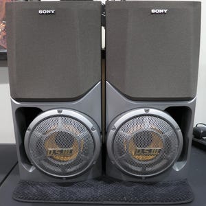 May include: Two gray Sony speakers with a silver base and mesh speaker covers. The speakers have the word "SONY" printed on the top. The speaker covers have the text "D.S.III" printed on them.