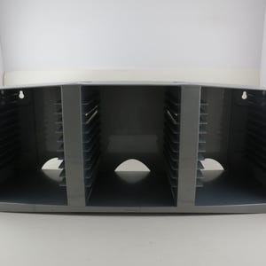 May include: A gray plastic media organizer with three compartments. Each compartment has vertical dividers for storage. The organizer has a curved front and two holes at the bottom. It is designed to hold CDs or DVDs.