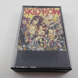 May include: A cassette tape with a black case and a colourful image of a band called "Skid Row". The image features five cartoon figures with exaggerated features, including a guitarist, a drummer, and a singer.
