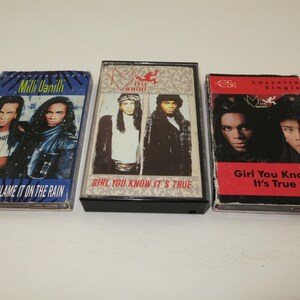May include: Three Milli Vanilli cassette tapes. The first is blue with "Blame It On The Rain" text. The second is black with "Girl You Know It's True" text. The third is red with "Girl You Know It's True" text.