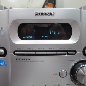 以下が含まれることがあります： デジタルディスプレイに1 1.41と表示された中央コンソール、5つのディスク選択ボタン、大きな音量調節ノブ、DSGX Dynamic Sound Generatorのロゴを備えたシルバーのソニー製ステレオシステム。両サイドにスピーカーが配置されています。