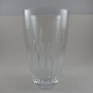 May include: A clear, tall glass vase with a flared top and a textured, patterned design. The vase has vertical lines that create a visual texture. The base of the vase has a diamond-like pattern.