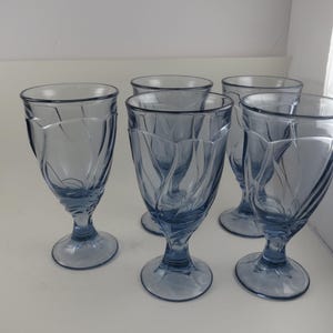 Pu&ograve; includere: Set di cinque bicchieri da dessert in vetro blu. Ogni bicchiere presenta una base a stelo e una coppa svasata con un motivo a spirale verticale. I bicchieri sono disposti su una superficie bianca.