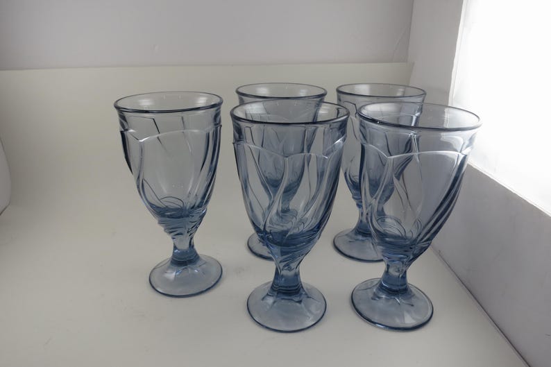 Pu&ograve; includere: Set di cinque bicchieri da dessert in vetro blu. Ogni bicchiere presenta una base a stelo e una coppa svasata con un motivo a spirale verticale. I bicchieri sono disposti su una superficie bianca.